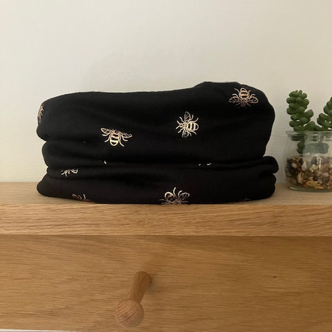 The Abella Snood Gold Bee Black is a wonderfully cosy and shimmering eye catching bee print snood