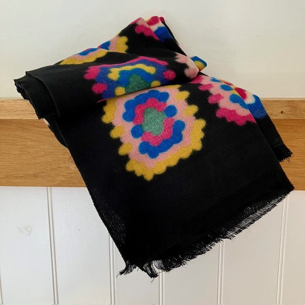 The Betsy Scarf has a black background with a stunning multicoloured crochet squares effect pattern 