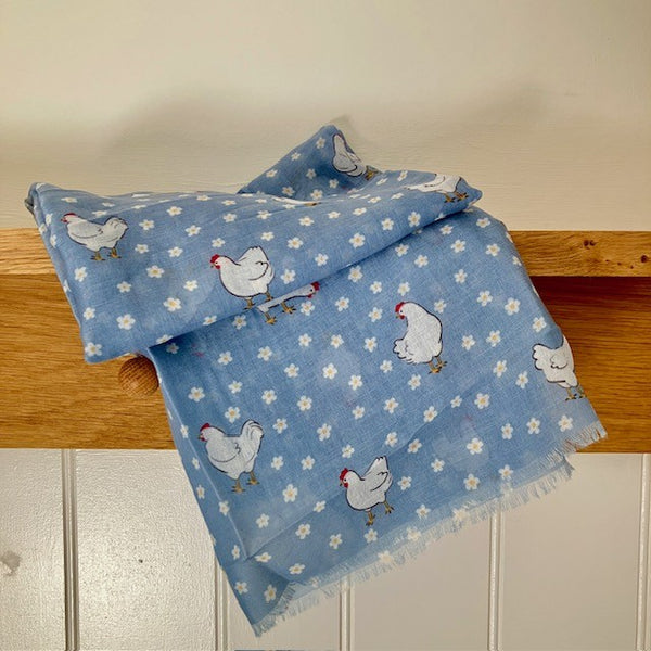 The Henrietta Scarf Blue has a repeating pattern of little white daisies and white chickens