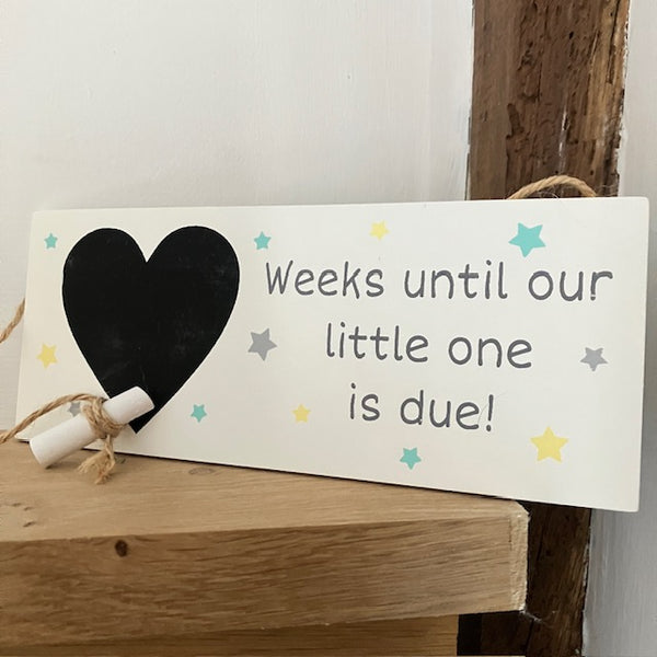 Wooden sign with a heart and text about weeks until baby is due, on a wooden surface.