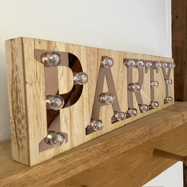 The Copper and Wood 'PARTY' Light Up Sign is made of wood, with copper letters and small plastic bulbs.