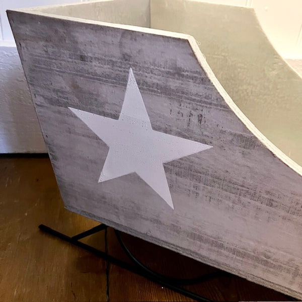 Up close of the grey/ white washed wooden sleigh with a white Scandi star, featuring metal details and a rustic finish