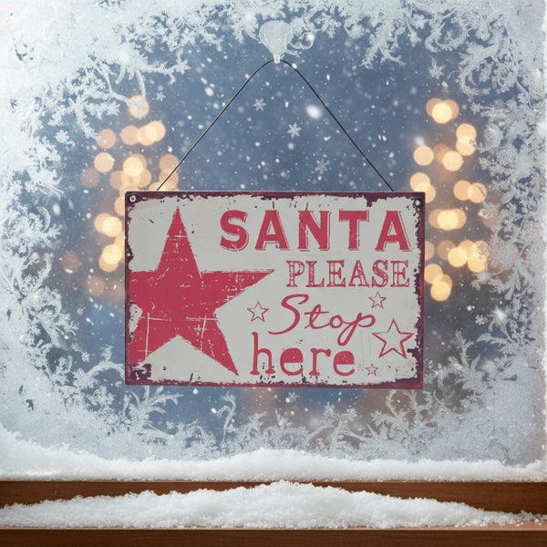 A retro red and white 'Santa Please Stop Here' sign made of tin, with a pinkish red tint and star decorations.